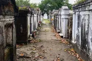 The image shows a pathway flanked by rows of weathered above-ground tombs or mausoleums in what appears to be an old cemetery.