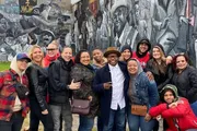 A group of cheerful people is posing for a photo in front of a grayscale mural.
