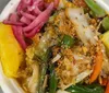 The image shows a bowl filled with a colorful mix of foods including pickled red onions green beans carrots pineapple a lime wedge and topped with crispy fried onions
