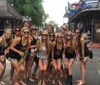 A group of happy women are posing together on a city street several of them wearing matching tank tops suggesting a group celebration or event