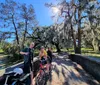 Three people are enjoying a sunny day outdoors on a bridge surrounded by trees draped with Spanish moss with two bicycles resting beside them