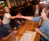 A group of people is having a good time at a pub or a restaurant where one person is cheerfully handing over a drink to another across the table