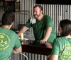 A group of people wearing matching green shirts advertising 504 Rum New Orleans are chatting and smiling around a bar area with a metal backdrop