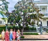 Five individuals are posing on a sidewalk in front of a classical residential building with a large magnolia tree in the foreground