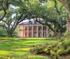 A stately historic mansion stands surrounded by sprawling live oak trees with lush greenery in a serene park-like setting