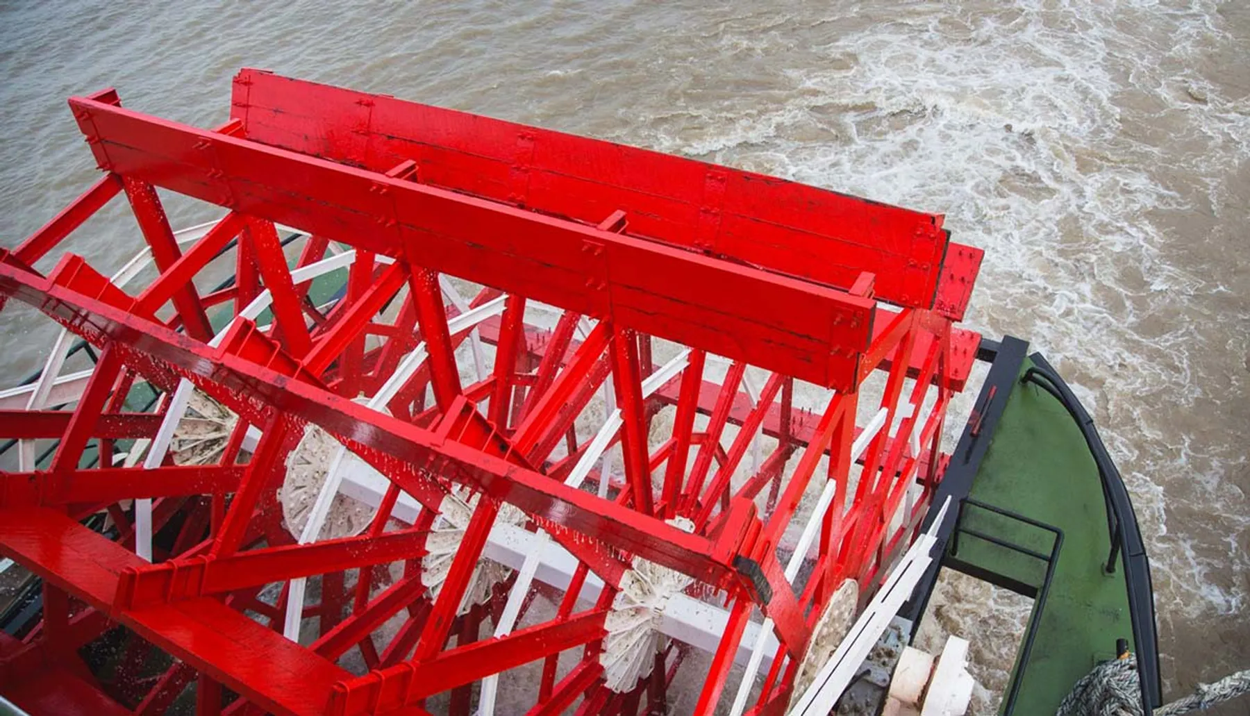 A vivid red structure, possibly a part of a navigational marker or buoy, is partially submerged in churned, muddy waters, seen from above.