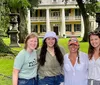 Four people are smiling for a photo in front of a classic two-story house with large columns and surrounded by trees