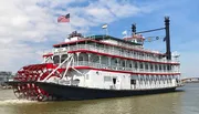 The image shows a classic multi-deck riverboat with a large red paddle wheel, named 