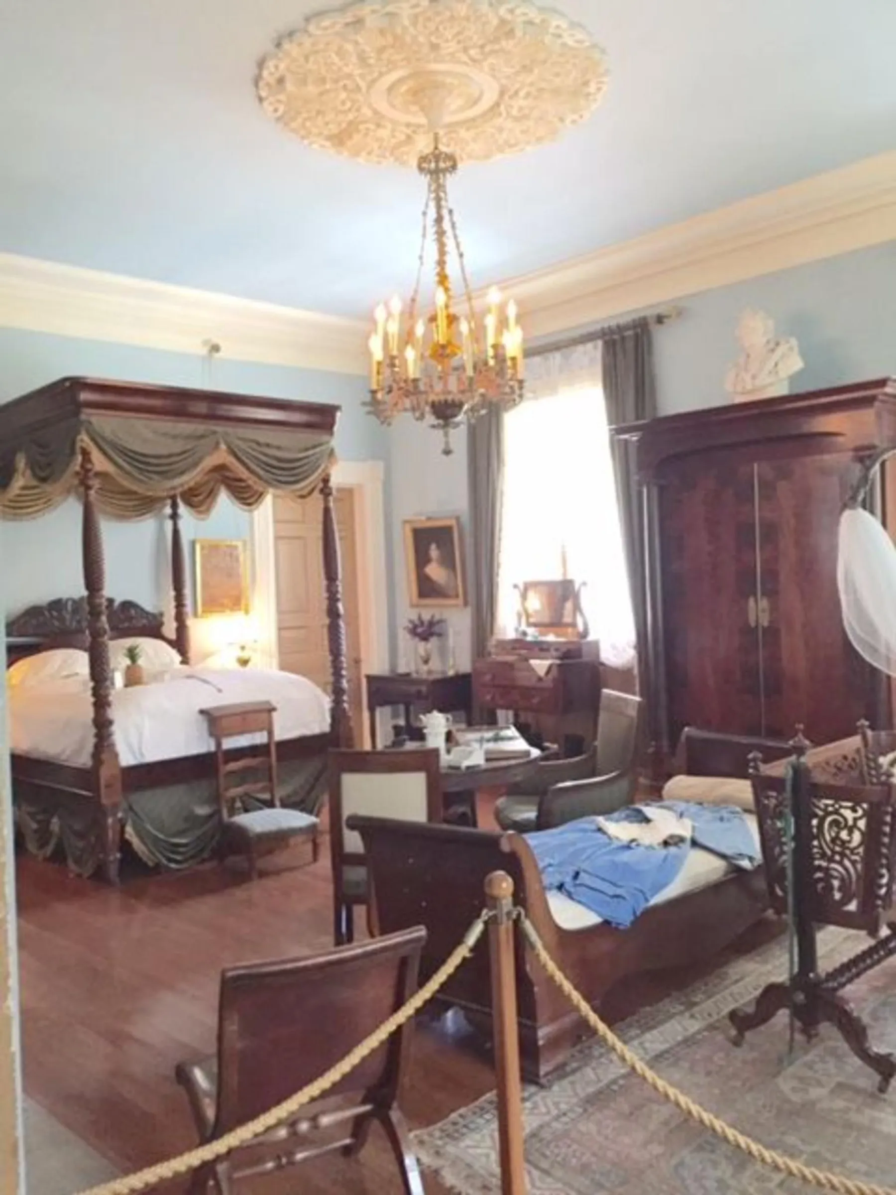 The image shows a Victorian-style bedroom with antique furniture, ornate decorations, and is cordoned off, suggesting it might be part of a museum or historic home tour.