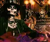 A person with skull face makeup is seated in an ornate chair with purple smoke around evoking a mystical or Gothic atmosphere