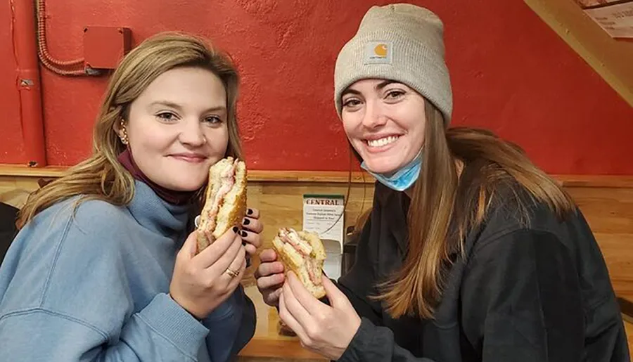 Two smiling women are holding up their sandwiches for the camera inside a casual dining establishment.