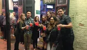 A group of people is posing for a photo on a street with drinks in hand, smiling and looking at the camera.