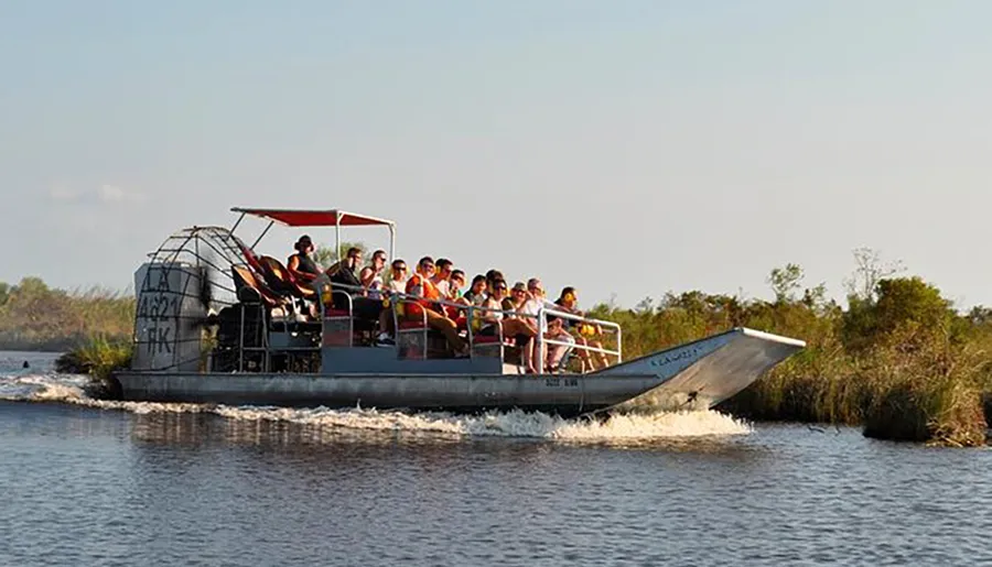 A group of people is enjoying a ride on an airboat through a waterway surrounded by grassy terrain, likely in a marsh or swamp area.