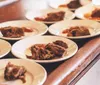 The image shows a series of white plates with portions of pulled pork neatly arranged on a wooden counter