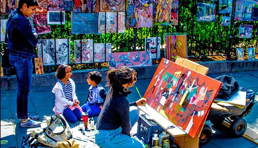An artist paints on a sunny day at an outdoor gallery while onlookers observe the art on display.