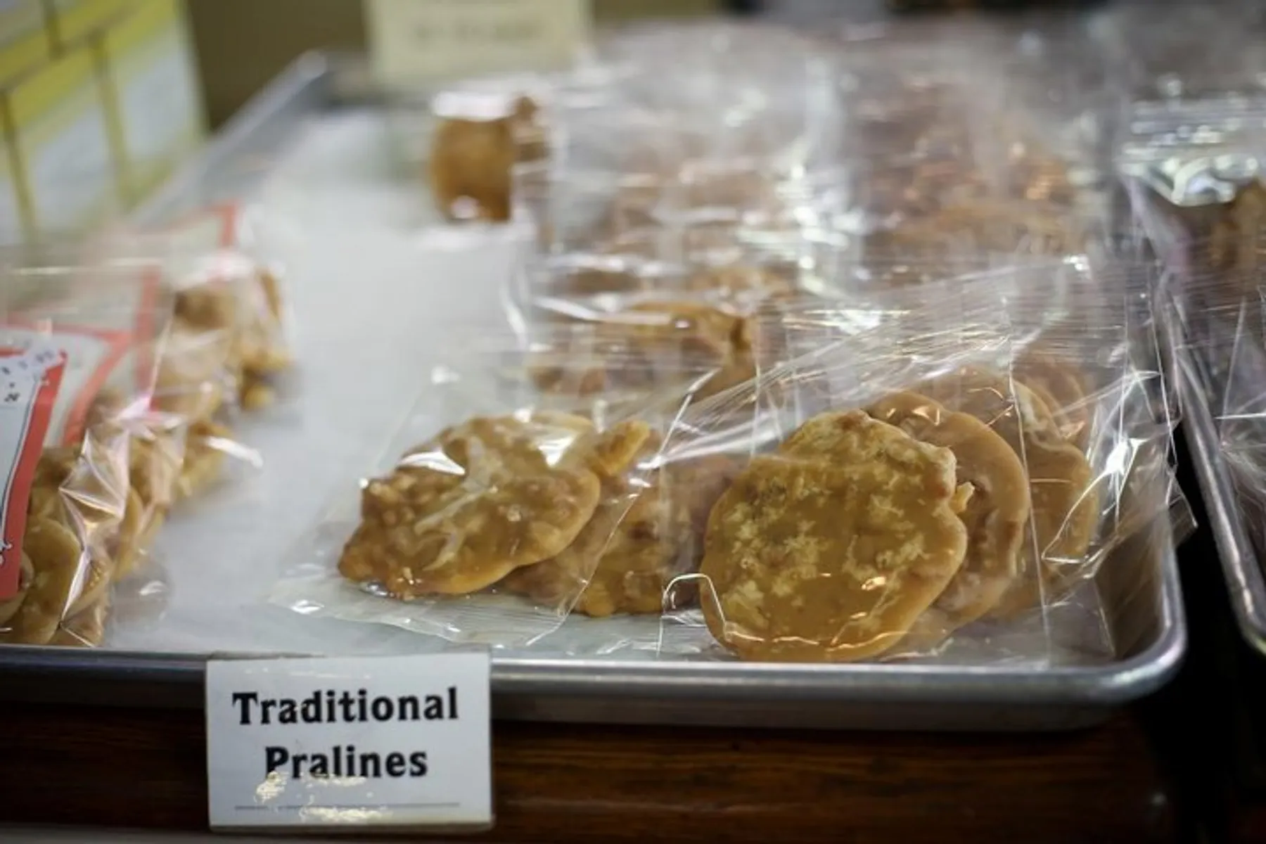 The image shows a tray of traditional pralines individually wrapped in plastic, displayed for sale with a label in front.