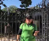 A person is standing in front of an ornate metal gate that appears to be the entrance to a cemetery or crypt gesturing with an open hand