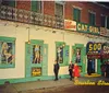 The image shows a lively vintage night scene on Bourbon Street with pedestrians walking past the colorful faade of the 500 Club featuring posters of the entertainer Lilly Christine the Cat Girl