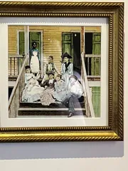 The image shows a framed, colorized photograph of a group of seven people, likely a family, posing together on a wooden porch, conveying a vintage ambiance.