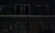This is a poorly lit nocturnal photograph showing the facade of a building with a balcony and arched windows, and a person on the sidewalk is visible on the right side of the image.
