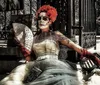 A person is dressed in an elaborate costume with a skull face makeup reminiscent of the Mexican La Catrina sitting on a bench with a fan in hand evoking a scene from the Day of the Dead celebrations