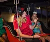 A group of individuals appears to be on a bus or tram ride at night with a person in a red shirt and black hat seemingly acting as a tour guide or entertainer