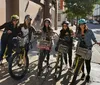 A group of five smiling people wearing helmets are posing with rental bicycles on a sunny city street