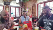 Three people are enjoying a moment of laughter and conversation at a casual dining establishment with brick walls and sports-themed decor.