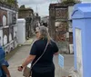 Two women are walking and conversing in a historic cemetery with above-ground tombs and weathered brickwork