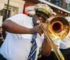 A trombone player performs enthusiastically on the street alongside other brass band members during what appears to be a lively parade or street festival