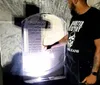 A person wearing a t-shirt with a skull design is pointing at an inscription on a tombstone during nighttime