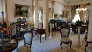 This image shows an opulent room furnished with an elegant vintage decor, featuring ornate chairs, classical sculptures, a fireplace, and elaborate artworks.