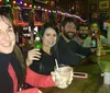 A group of friends is smiling and holding drinks at a bar decorated with festive lights