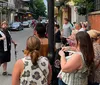 A man wearing a hat and a vest is enthusiastically giving a tour to a group of people on a picturesque street at dusk