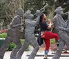 A person is playfully interacting with a sculpture of a jazz band by pretending to sing along with the musicians