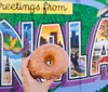 A person is holding up a glazed donut against a colorful mural that says Greetings from NOLA with the donut strategically placed to complete the O in NOLA
