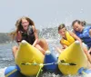 Three children are joyously riding a yellow inflatable banana boat on a sunny day splashing through the water