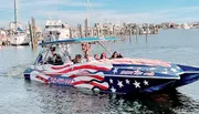 A group of people enjoy a ride on a speedboat adorned with an American flag design in a marina.