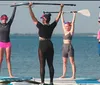 Four individuals are standing on paddleboards in a body of water each holding a paddle overhead with a clear sky in the background