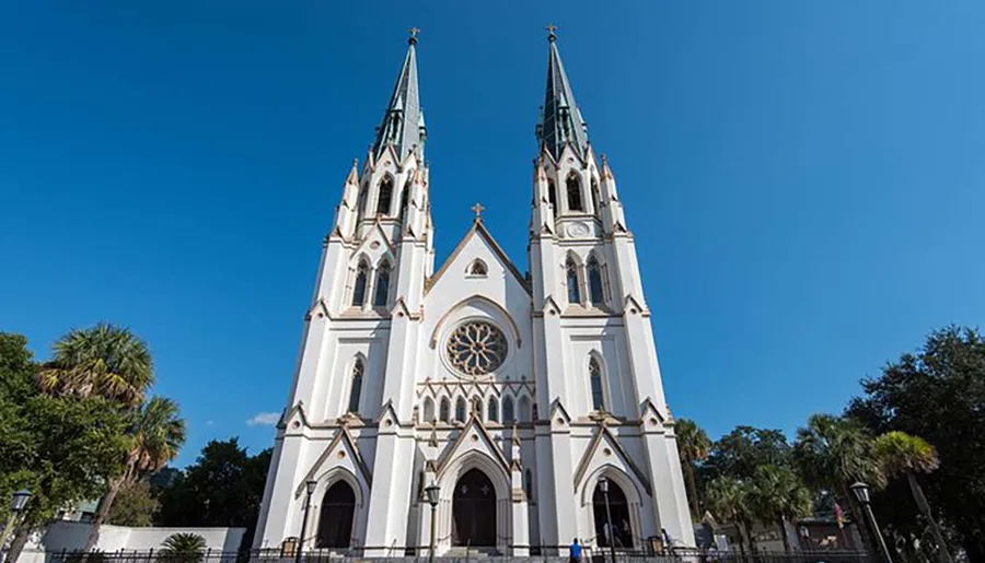 The image shows a white gothic revival style church with two sharp spires against a clear blue sky.