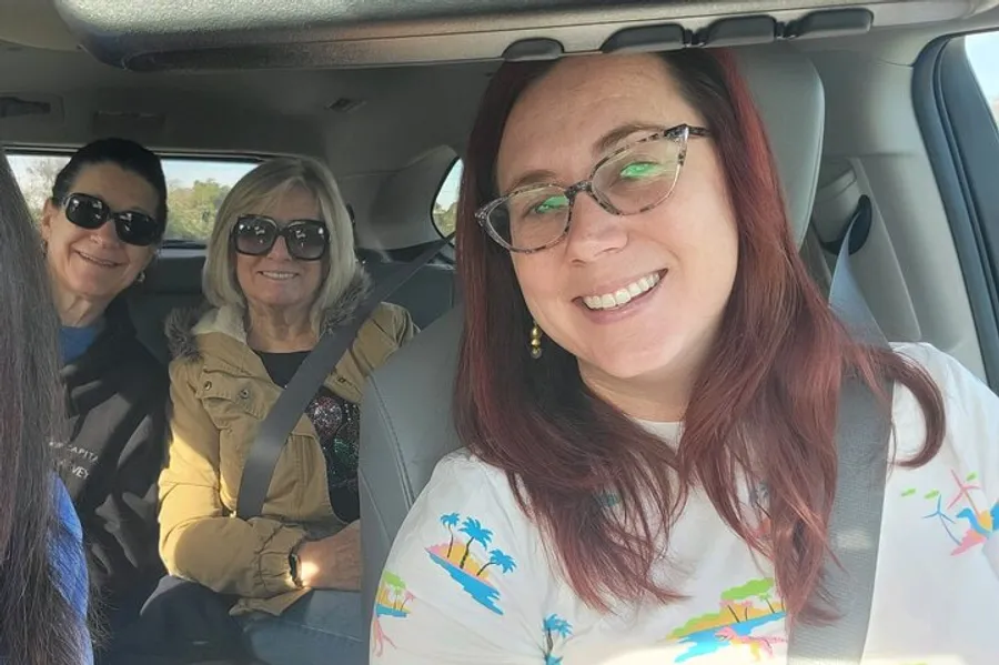 Three women are smiling for a selfie inside a car during the daytime.