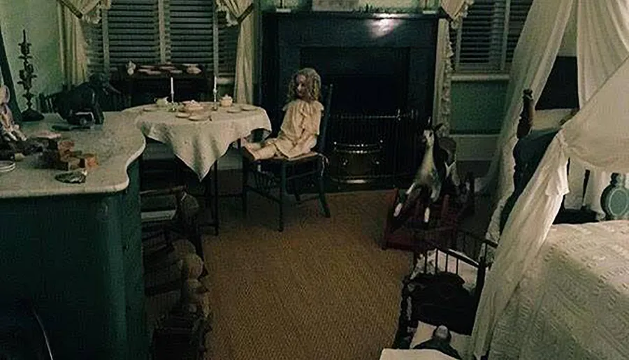 The image shows a dimly lit vintage room with a doll seated at a table, creating a creepy or haunted atmosphere.