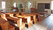 This image shows a vintage classroom setting with wooden desks, a blackboard, and traditional school furnishings, suggesting a historical or educational exhibit.