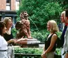 Four individuals are engaged in a conversation in front of a bronze statue of a lion in a park-like setting