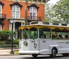 A trolley bus marked Old Savannah Tours is driving past an ornate brick building with balconies suggesting a historical tour in progress