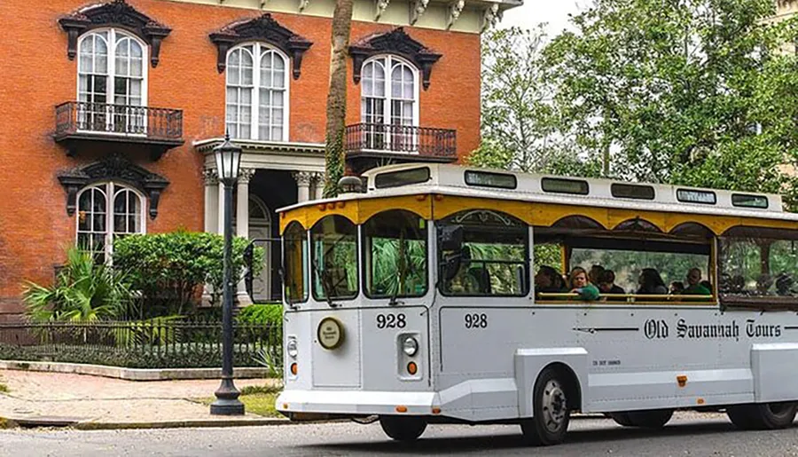 A trolley bus marked Old Savannah Tours is driving past an ornate brick building with balconies, suggesting a historical tour in progress.