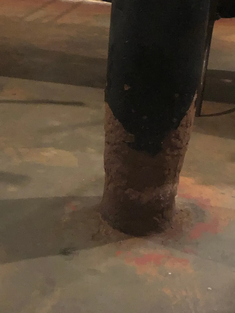 The image depicts a corroded metal pole with visible rust at the base where it meets a concrete floor.