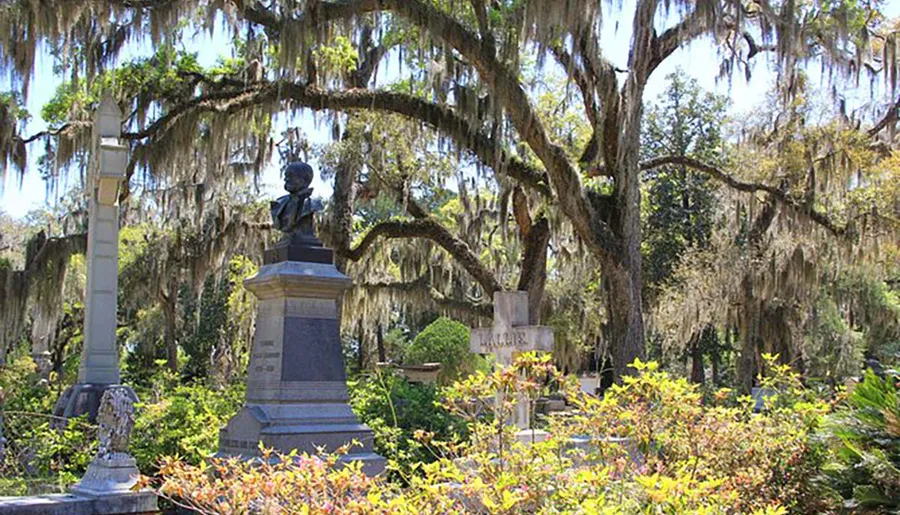 This image shows a tranquil cemetery adorned with Spanish moss hanging from ancient oak trees, memorial statues, and bright floral foliage.