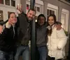 Four people are posing happily for a photo at night on an urban street with one of them raising a glass in a toasting gesture