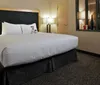 The image shows a neatly arranged hotel room with a large bed nightstands lamps and a decorative mirror reflecting an image on the opposite wall
